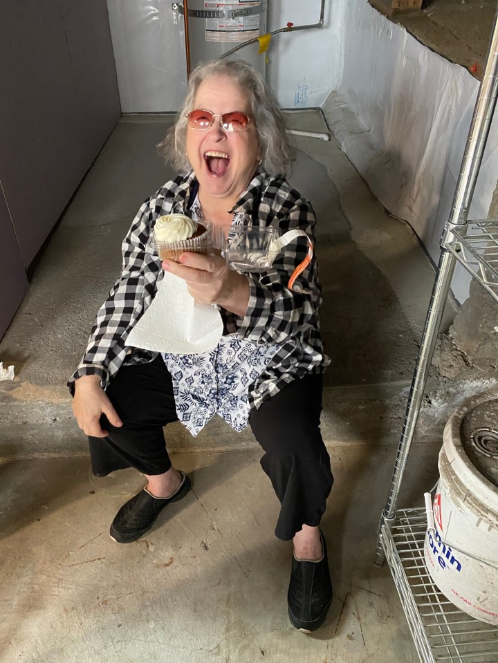 An elderly greek woman holding a cupcake and laughing